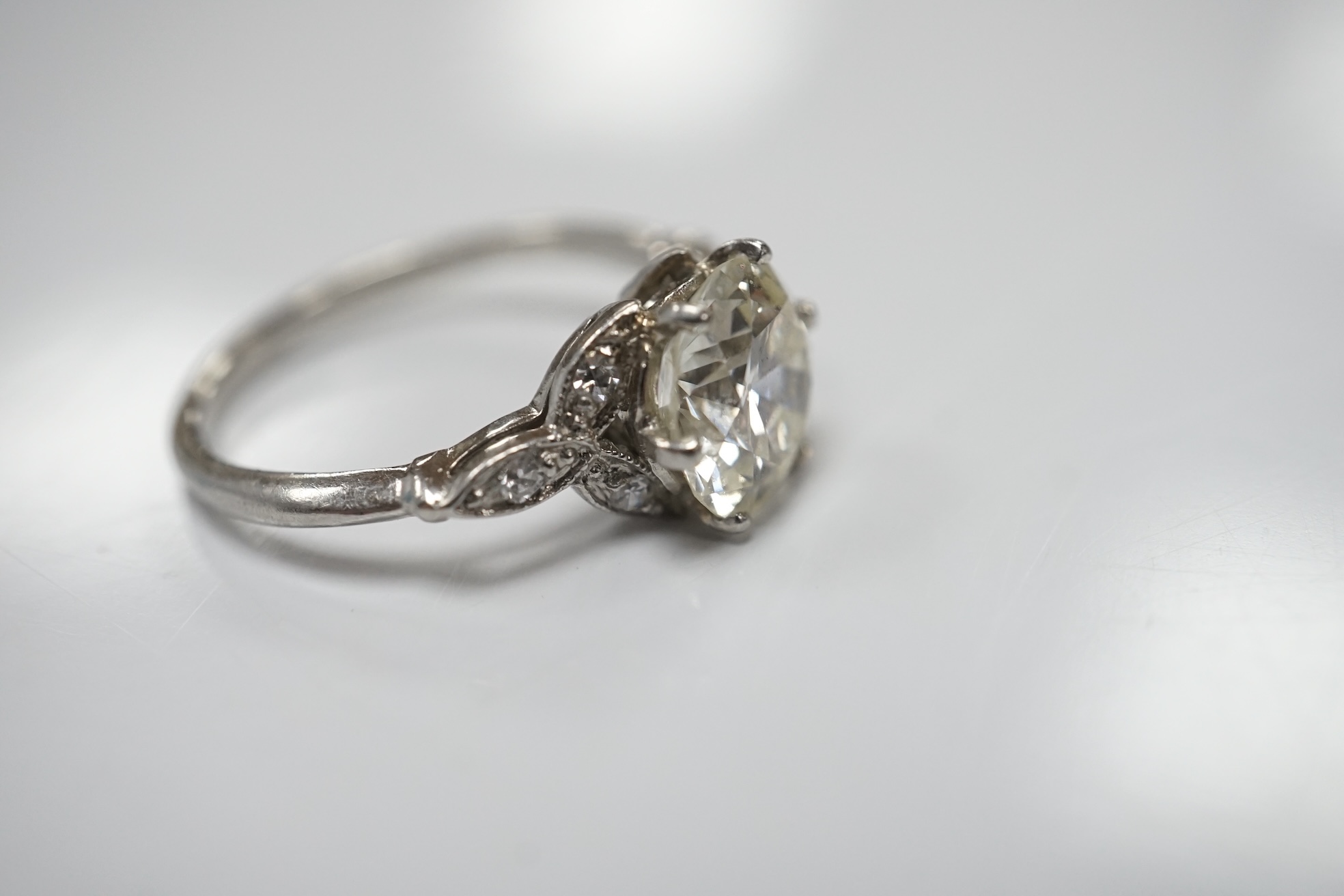 A platinum and single stone diamond set ring, with six stone diamond chip set foliate shoulders, the centre stone weighing 1.60ct, size H/I, gross weight 3.1 grams. Condition - fair